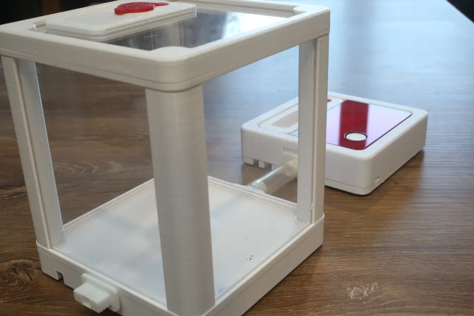 Show: An Acrylic Arena joined by a clear tube to a Hybrid Nest Air with its red top on, on a wooden table